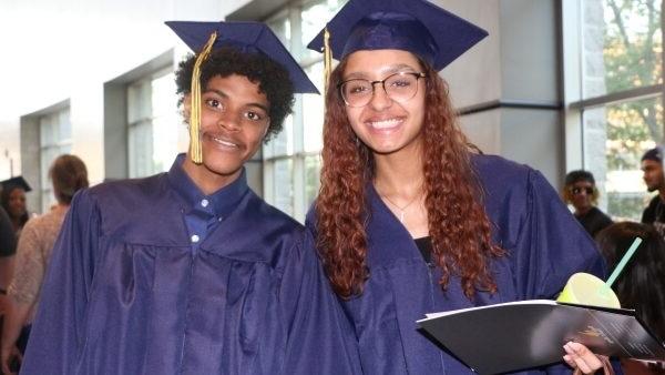 2 grads in caps & gowns smiling at camera